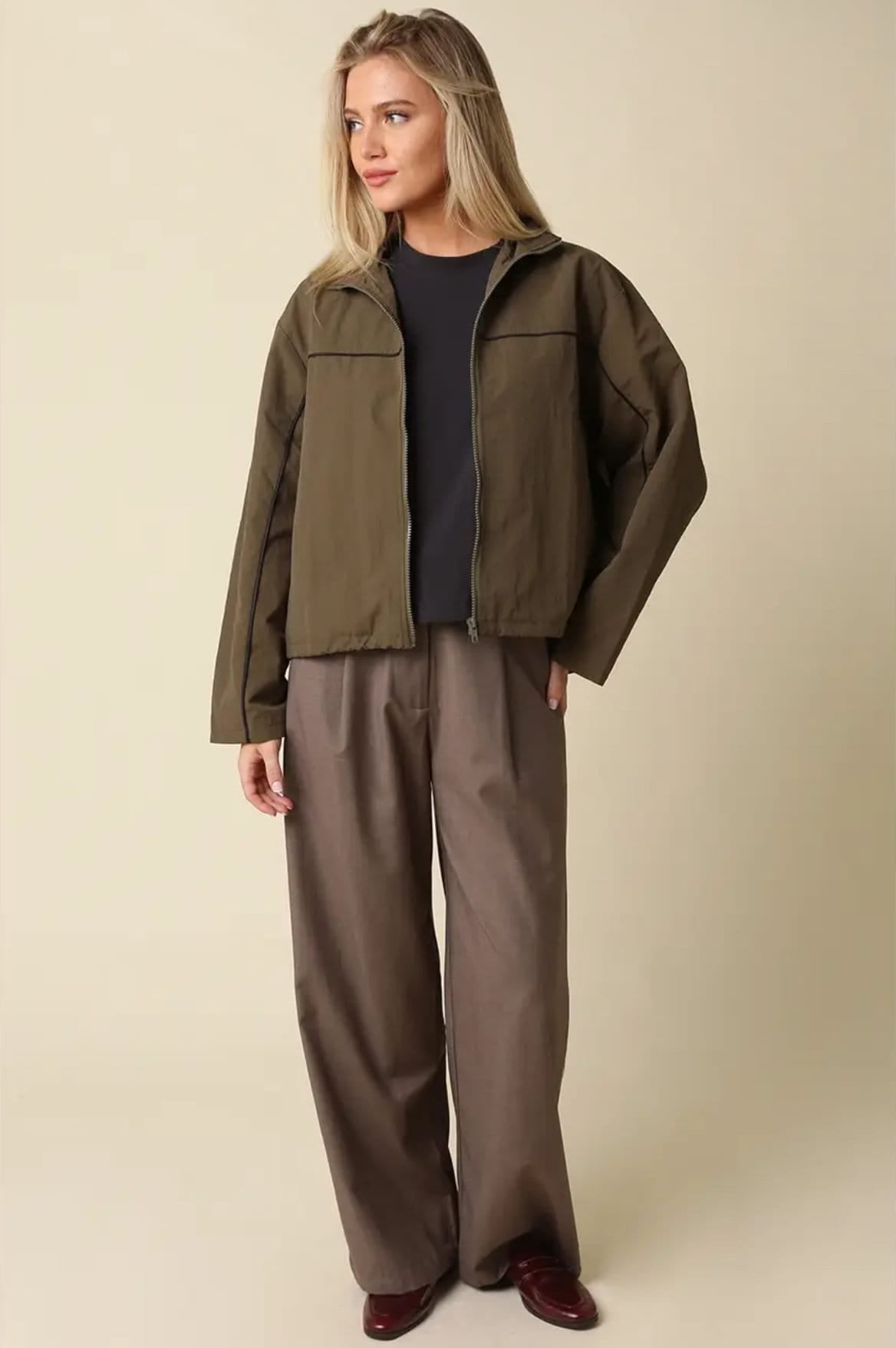 Woman wearing olive green Alina piped zip-up jacket with brown wide-leg trousers and burgundy loafers